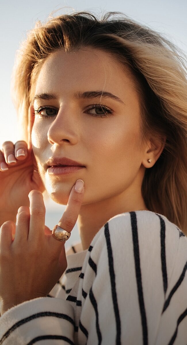 Woman touching her face against sunlit background.